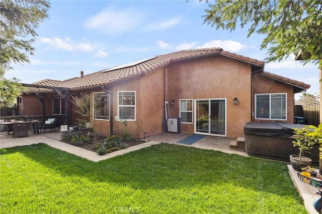 rear view of property featuring stucco siding, a lawn, a hot tub, and a patio area