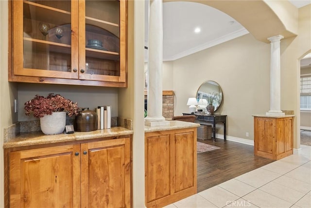 bar with crown molding, baseboards, light tile patterned floors, arched walkways, and ornate columns