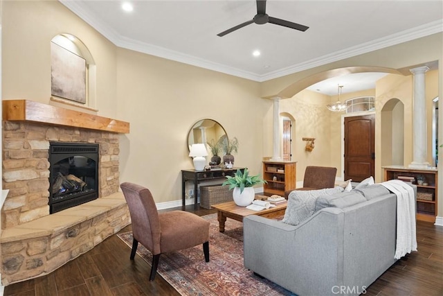 living area with dark wood-style floors, a stone fireplace, crown molding, and baseboards