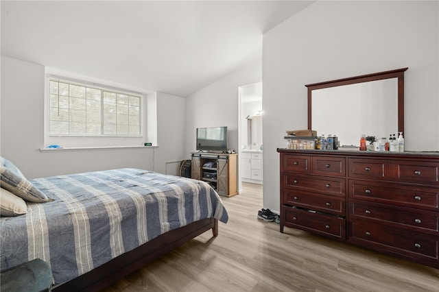 bedroom featuring ensuite bath, light wood-style floors, and lofted ceiling