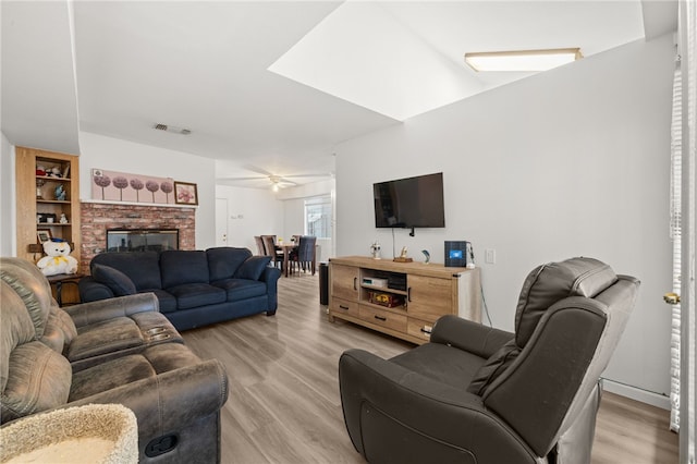 living area with light wood-type flooring, visible vents, a ceiling fan, and a fireplace