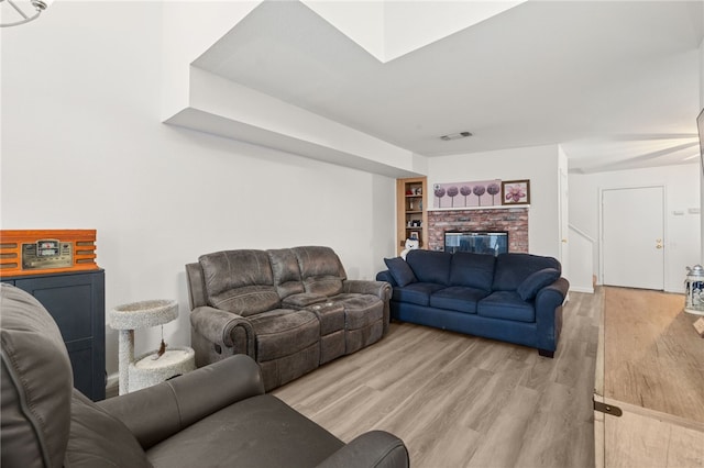 living room featuring light wood finished floors, visible vents, a brick fireplace, and built in features