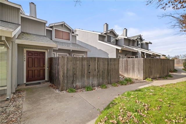 exterior space with a fenced front yard and roof with shingles