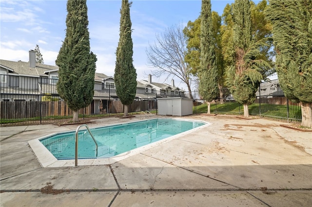 community pool with an outdoor structure, a fenced backyard, a shed, and a patio area