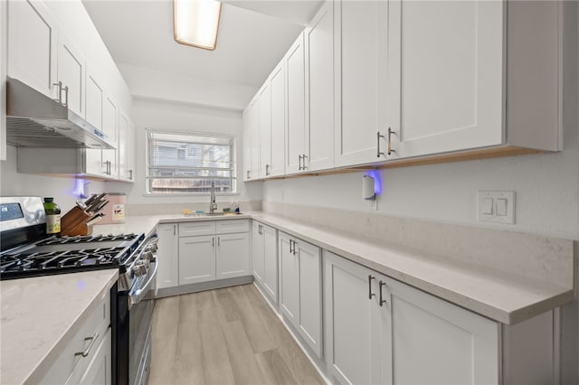 kitchen featuring under cabinet range hood, gas range, white cabinets, and light wood finished floors