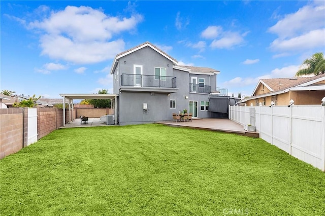 rear view of house with stucco siding, a lawn, a fenced backyard, a balcony, and a patio area