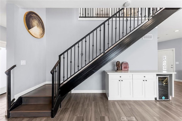 stairs featuring beverage cooler, visible vents, baseboards, and wood finished floors