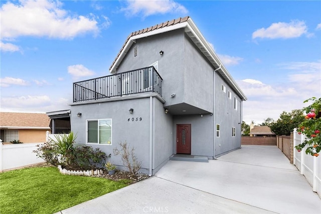 rear view of house with fence, stucco siding, a lawn, a balcony, and a patio area