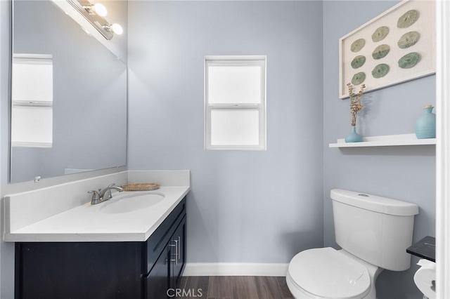 half bath featuring toilet, vanity, baseboards, and wood finished floors