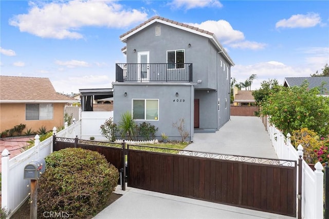 view of front of house featuring a fenced front yard, stucco siding, a balcony, and a gate