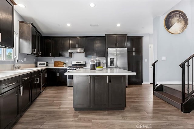 kitchen with visible vents, a sink, stainless steel appliances, under cabinet range hood, and a center island