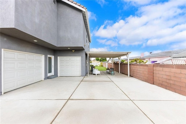 view of property exterior with stucco siding, driveway, fence, an attached garage, and a carport