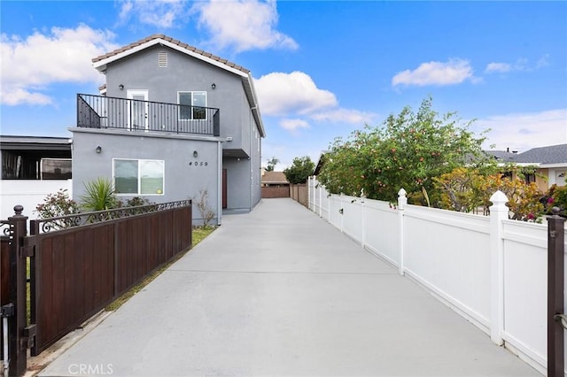 view of side of home featuring a fenced front yard, a tiled roof, stucco siding, a balcony, and a gate