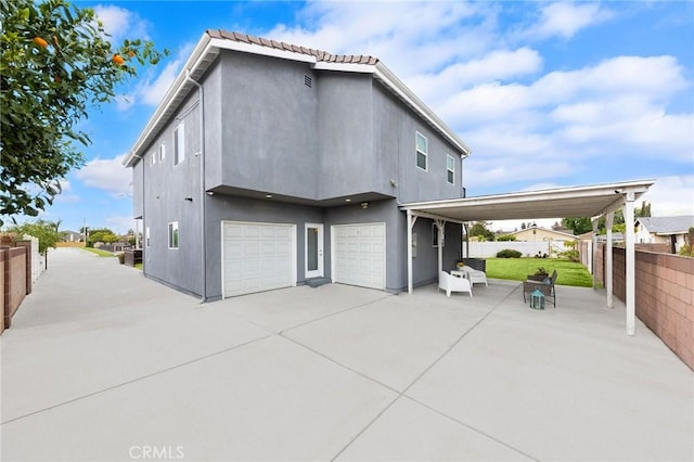 rear view of house featuring a garage, stucco siding, and fence