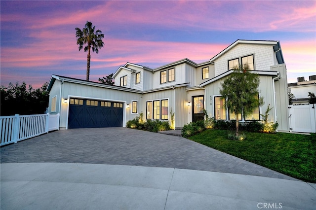 modern farmhouse featuring a gate, decorative driveway, fence, a yard, and an attached garage