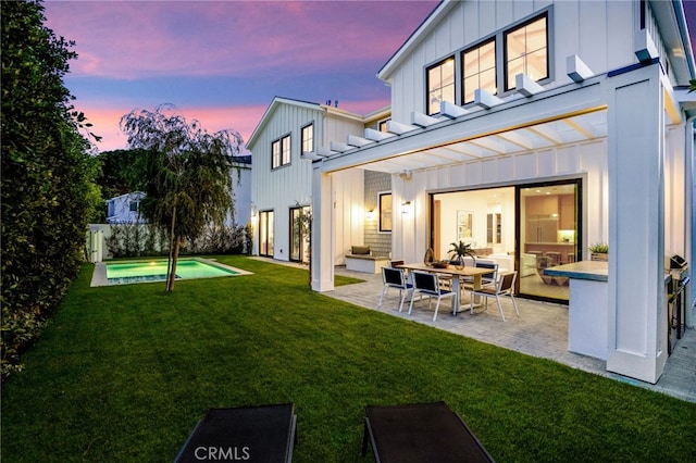 back of property at dusk featuring an outdoor pool, board and batten siding, a yard, and a patio