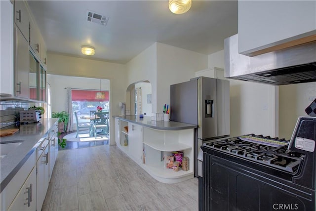 kitchen with visible vents, open shelves, arched walkways, white cabinets, and stainless steel fridge