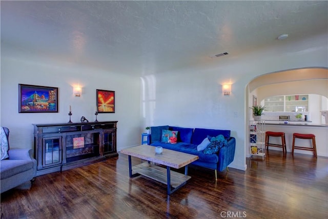 living room featuring a textured ceiling, wood finished floors, visible vents, and arched walkways