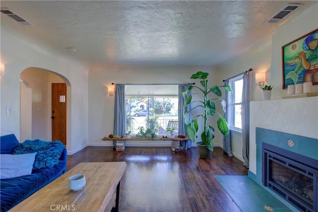 living room featuring visible vents, arched walkways, wood finished floors, and a tile fireplace