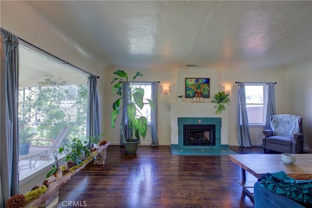 unfurnished living room featuring visible vents, a fireplace with flush hearth, a textured ceiling, wood finished floors, and baseboards