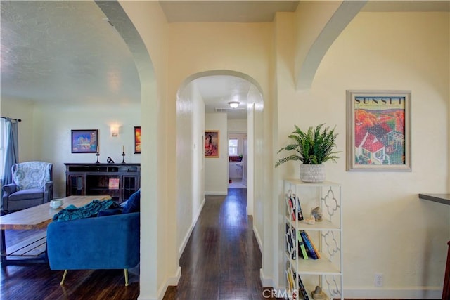 corridor featuring wood finished floors, arched walkways, and baseboards