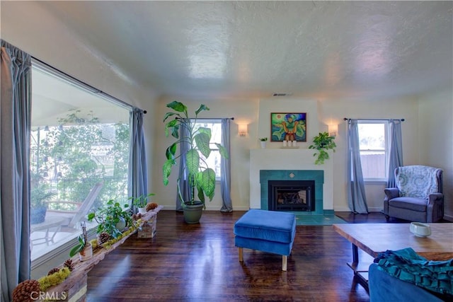 living room with visible vents, a textured ceiling, wood finished floors, baseboards, and a tile fireplace