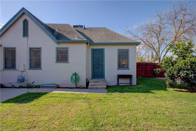 view of front of house featuring stucco siding, roof with shingles, a front yard, and fence