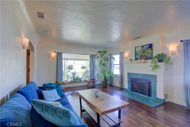 living room with a glass covered fireplace, wood finished floors, arched walkways, and visible vents