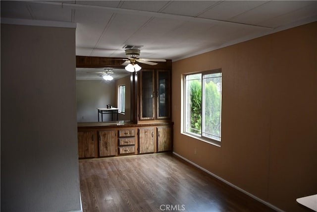 interior space with visible vents, glass insert cabinets, ceiling fan, baseboards, and wood finished floors