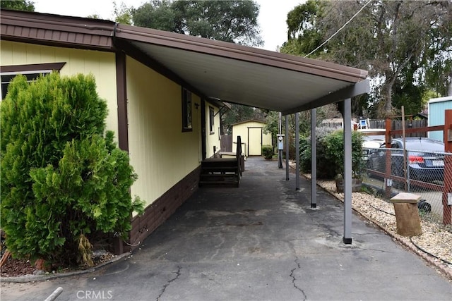 view of car parking featuring an attached carport, fence, and a shed