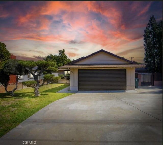 garage at dusk featuring a lawn, driveway, and fence