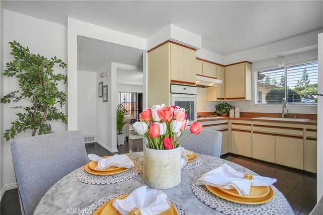 kitchen featuring cream cabinetry, under cabinet range hood, white oven, gas stovetop, and a sink