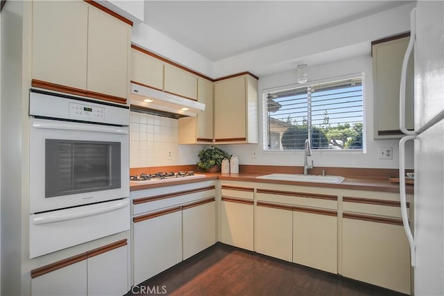 kitchen featuring white appliances, a sink, under cabinet range hood, cream cabinets, and a warming drawer