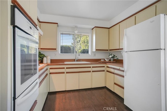 kitchen featuring dark wood-type flooring, cream cabinetry, white appliances, a warming drawer, and a sink