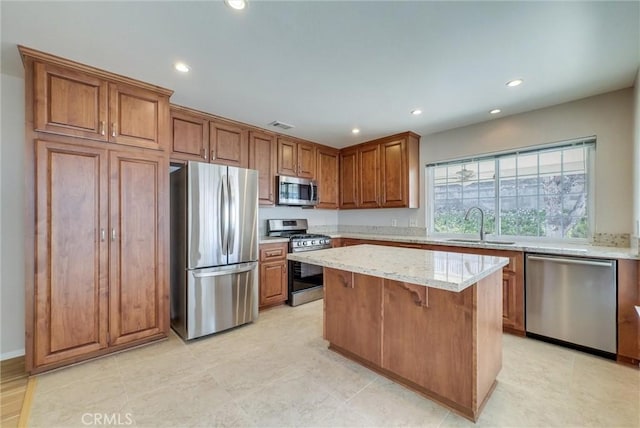 kitchen featuring a kitchen island, light stone countertops, brown cabinetry, stainless steel appliances, and a sink