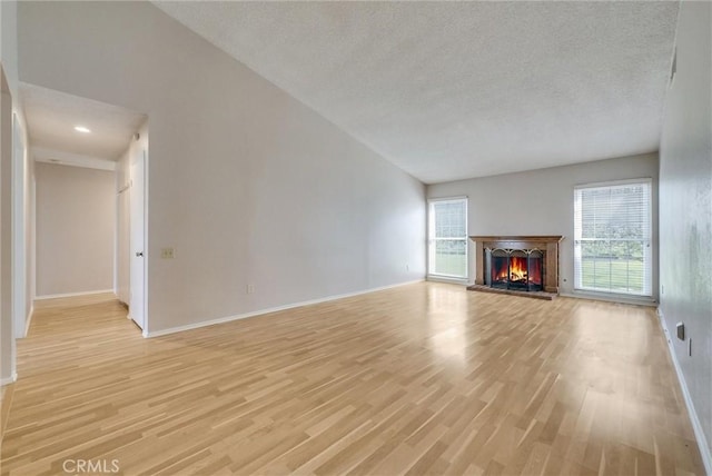 unfurnished living room with a wealth of natural light, a lit fireplace, and light wood-style flooring