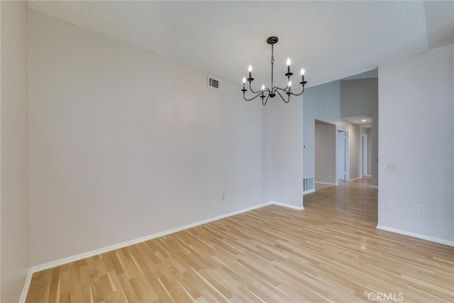 spare room with a notable chandelier, light wood-style flooring, baseboards, and visible vents