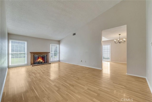 unfurnished living room featuring visible vents, light wood-type flooring, a warm lit fireplace, a notable chandelier, and a textured ceiling