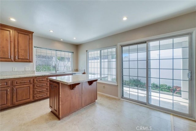 kitchen with a kitchen island, light stone counters, a kitchen breakfast bar, brown cabinetry, and a sink