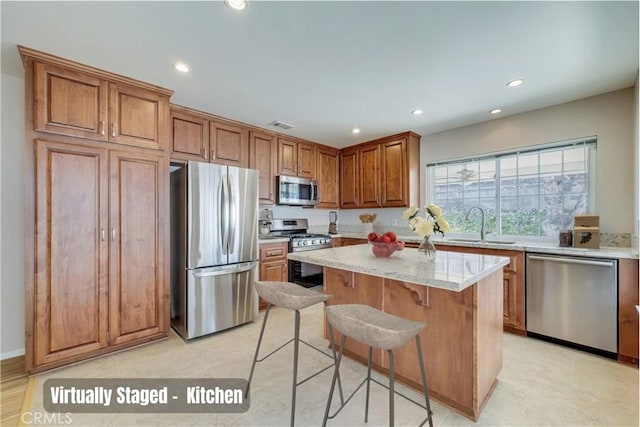 kitchen featuring a center island, a breakfast bar area, brown cabinets, stainless steel appliances, and a sink