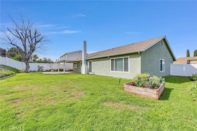 back of property with a garden, stucco siding, a yard, and a fenced backyard