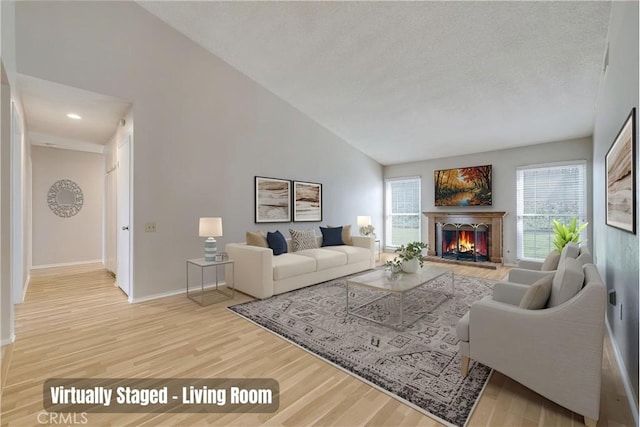 living area with high vaulted ceiling, a textured ceiling, wood finished floors, a lit fireplace, and baseboards