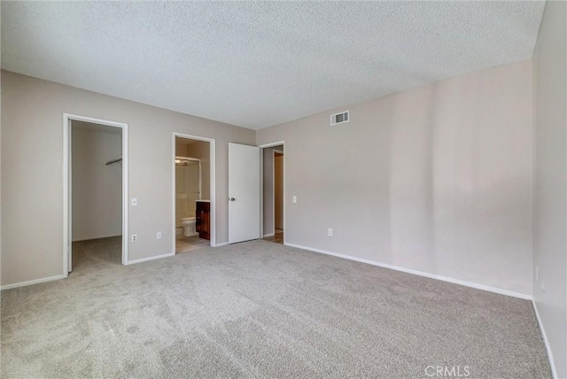 unfurnished bedroom with a spacious closet, visible vents, baseboards, carpet floors, and ensuite bath