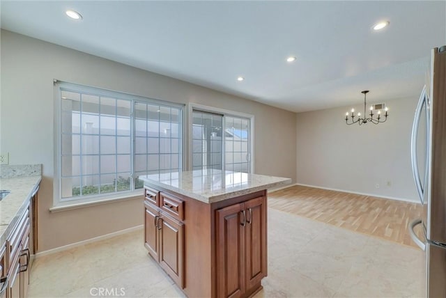 kitchen with light stone counters, recessed lighting, freestanding refrigerator, brown cabinets, and a chandelier