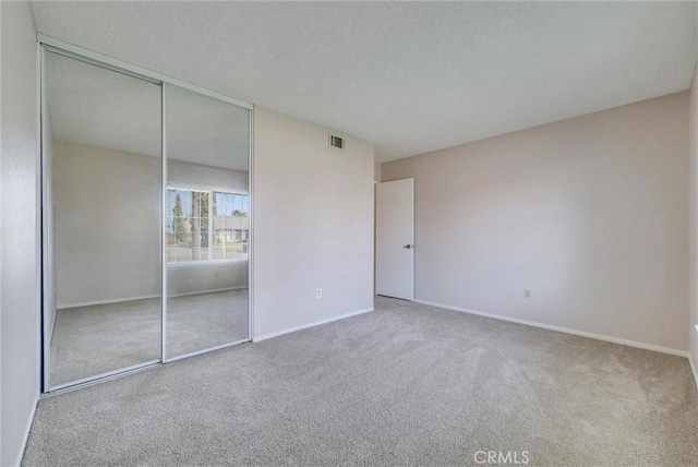 unfurnished bedroom featuring visible vents, a textured ceiling, a closet, carpet, and baseboards