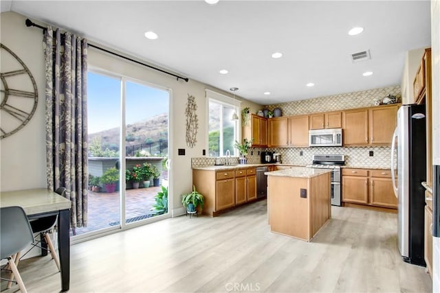 kitchen with visible vents, a kitchen island, light wood-style flooring, stainless steel appliances, and decorative backsplash