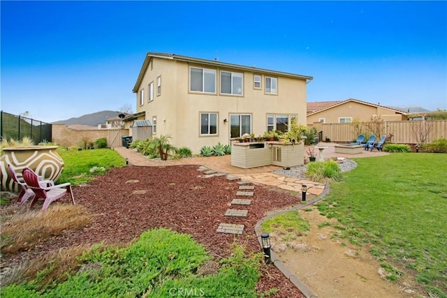 rear view of property with a yard, stucco siding, a fire pit, and a fenced backyard