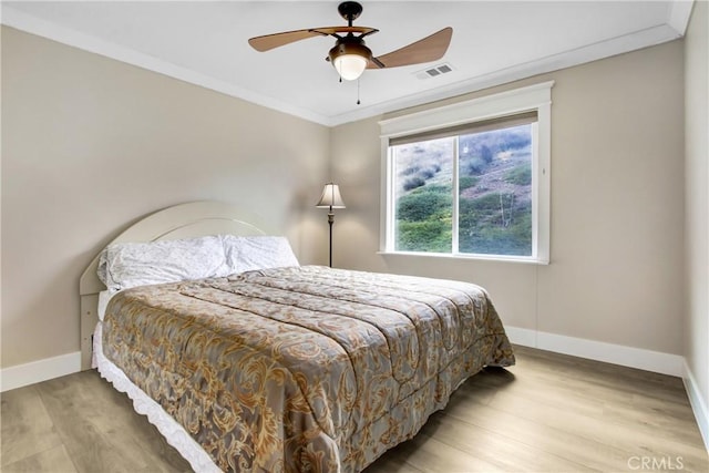 bedroom featuring a ceiling fan, baseboards, wood finished floors, visible vents, and ornamental molding