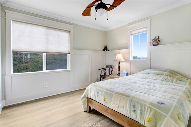 bedroom featuring ceiling fan, a wainscoted wall, ornamental molding, wood finished floors, and a decorative wall