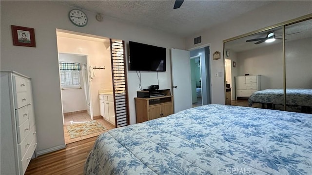 bedroom featuring visible vents, ensuite bathroom, a textured ceiling, wood finished floors, and ceiling fan